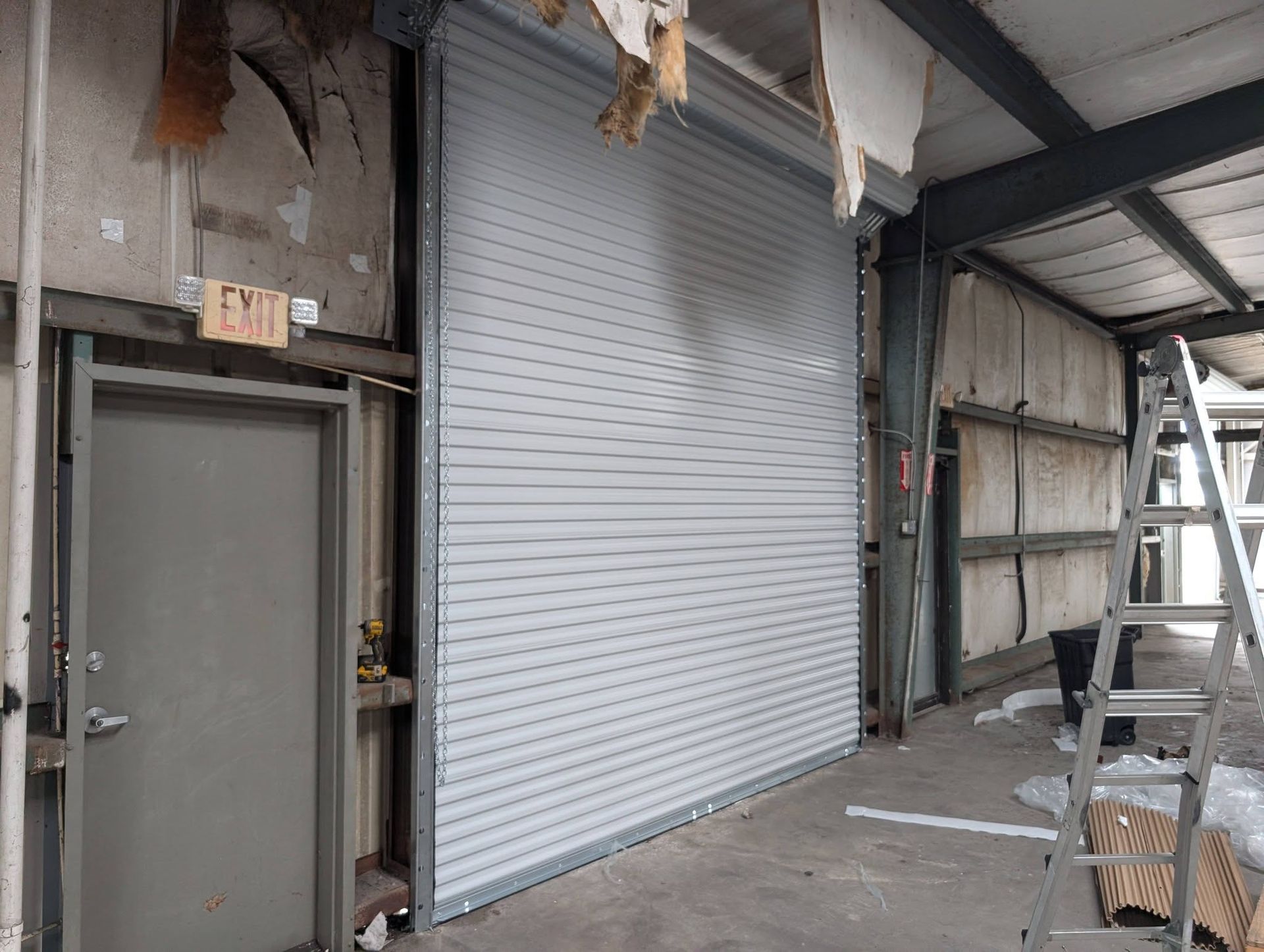 Interior view of a building under construction. A large gray roll-up door is closed next to a closed gray door. Interior view of a building under construction. A large gray roll-up door is closed next to a closed gray door.