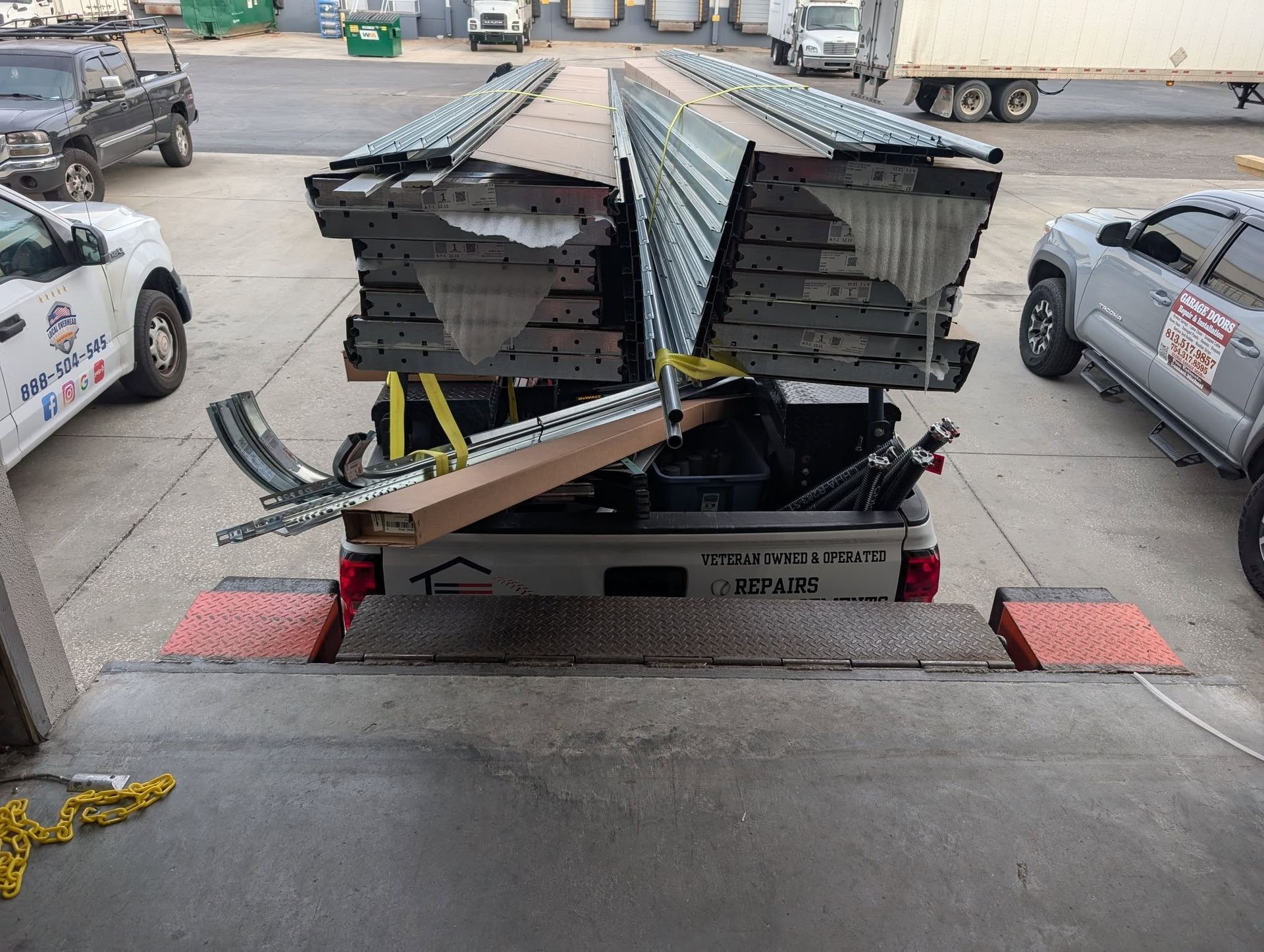 Truck bed loaded with metal components at a loading dock. Two trucks visible. Truck bed loaded with metal components at a loading dock. Two trucks visible.