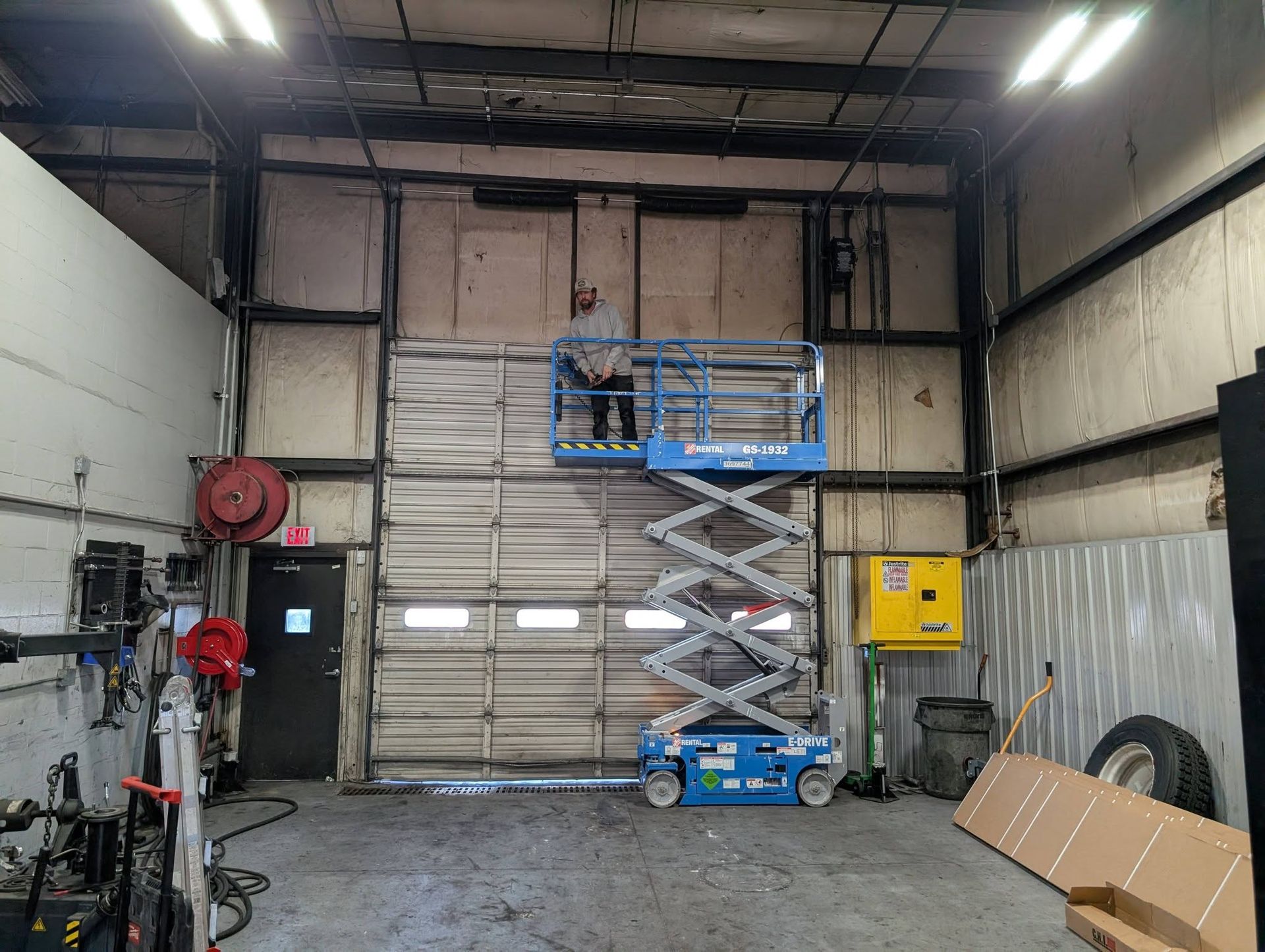 Person on lift working on wall above a closed garage door in a shop. Person on lift working on wall above a closed garage door in a shop.