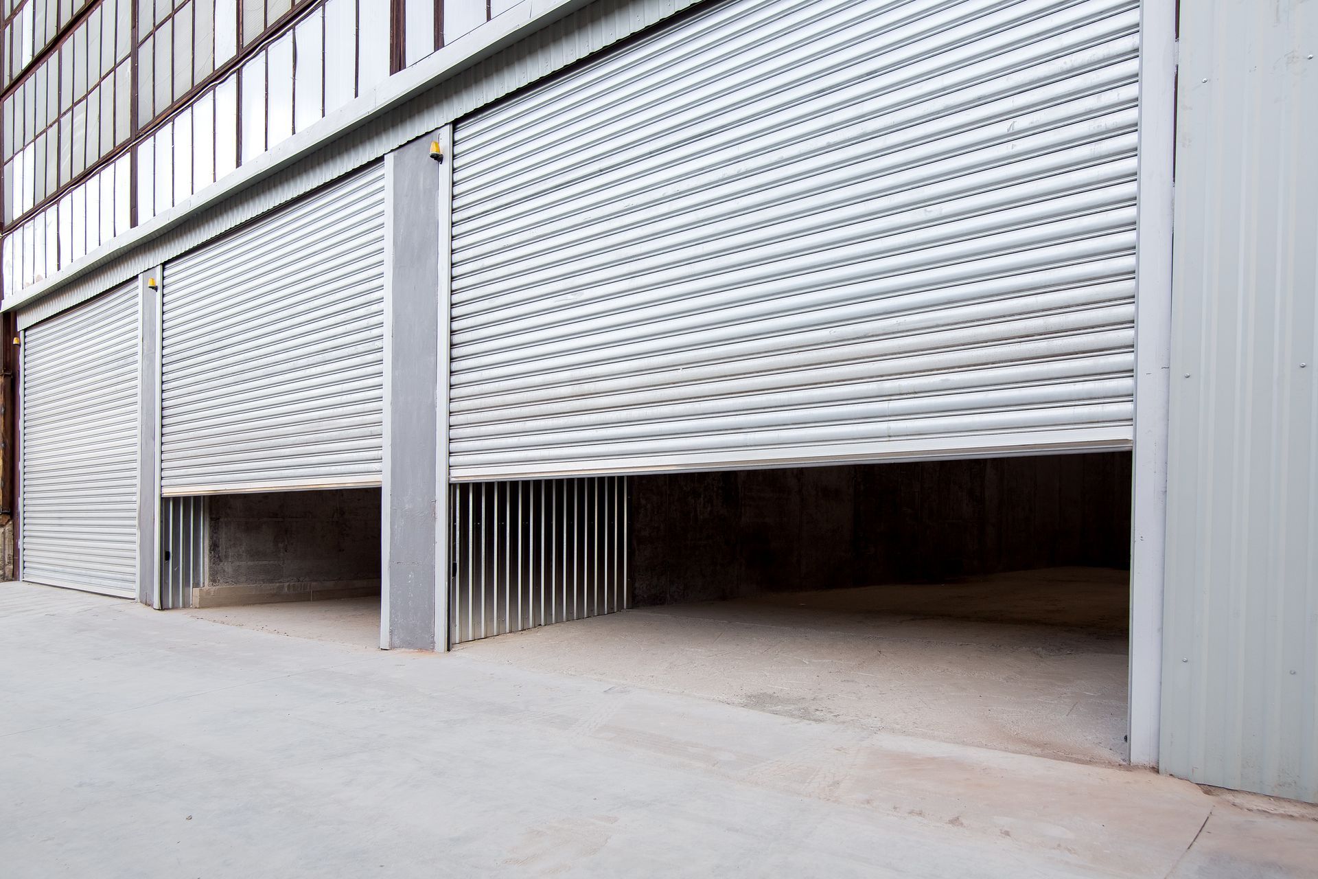 Open warehouse bay doors, silver metal, concrete floor.