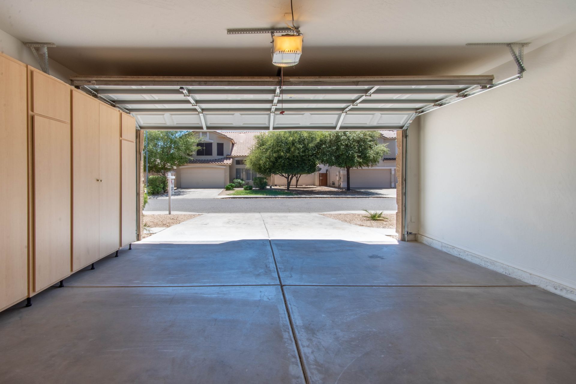 Empty garage with open door; view of a residential street with houses and trees. Empty garage with open door; view of a residential street with houses and trees.
