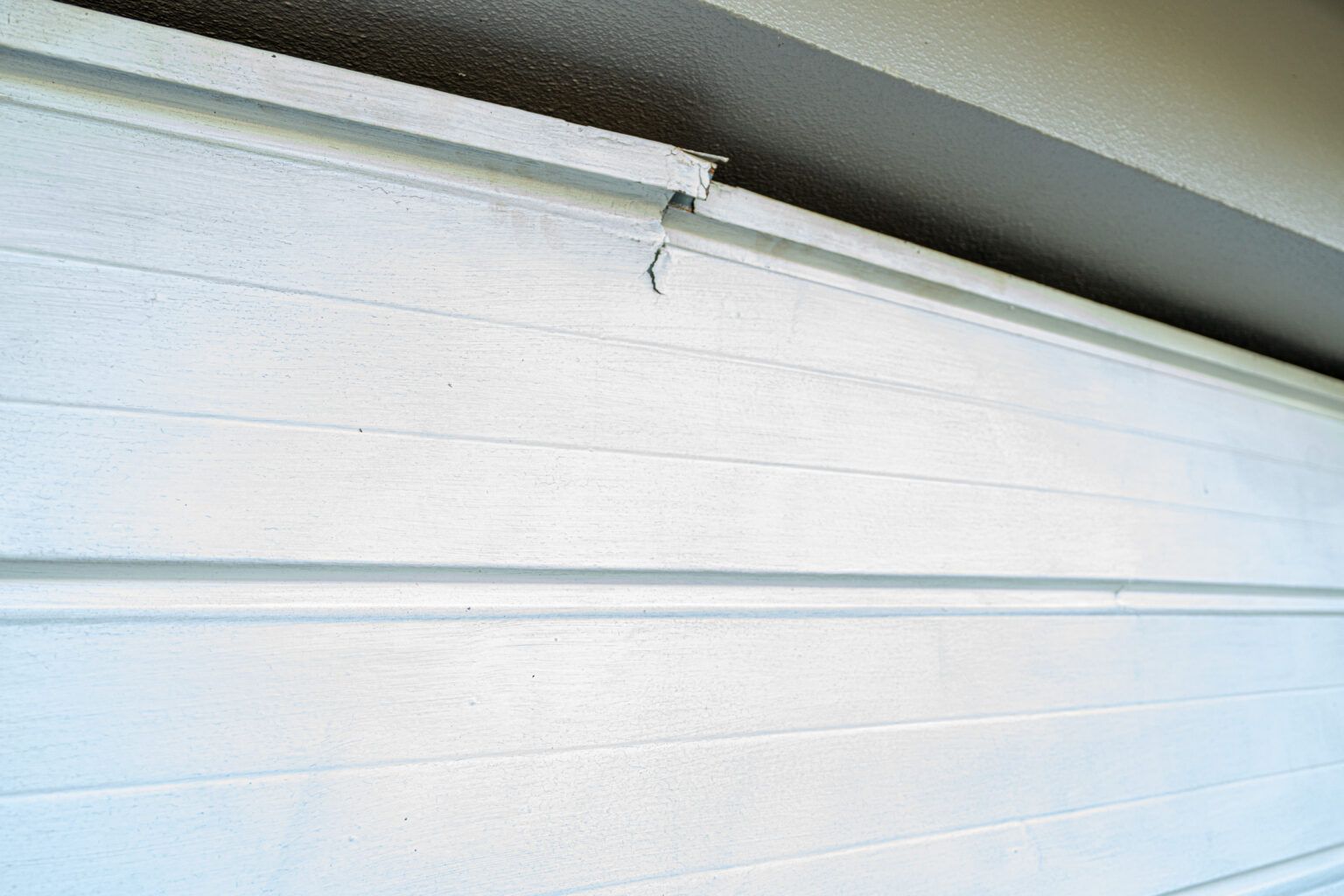 White garage door with visible damage near the top, possibly a crack or break.
