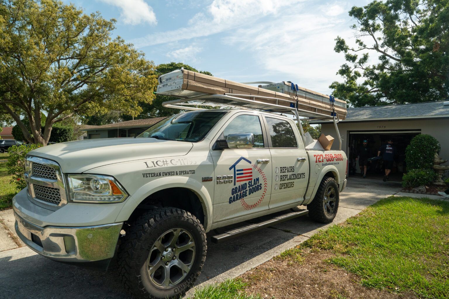 White pickup truck with ladder on top parked in a driveway; house and garage in the background.