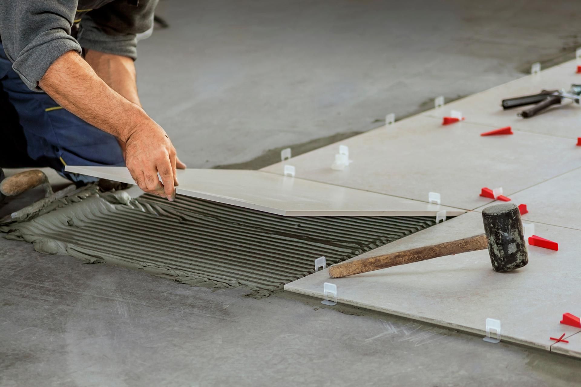 a man is laying tiles on the floor with a hammer .