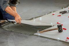 a man is laying tiles on the floor with a hammer .
