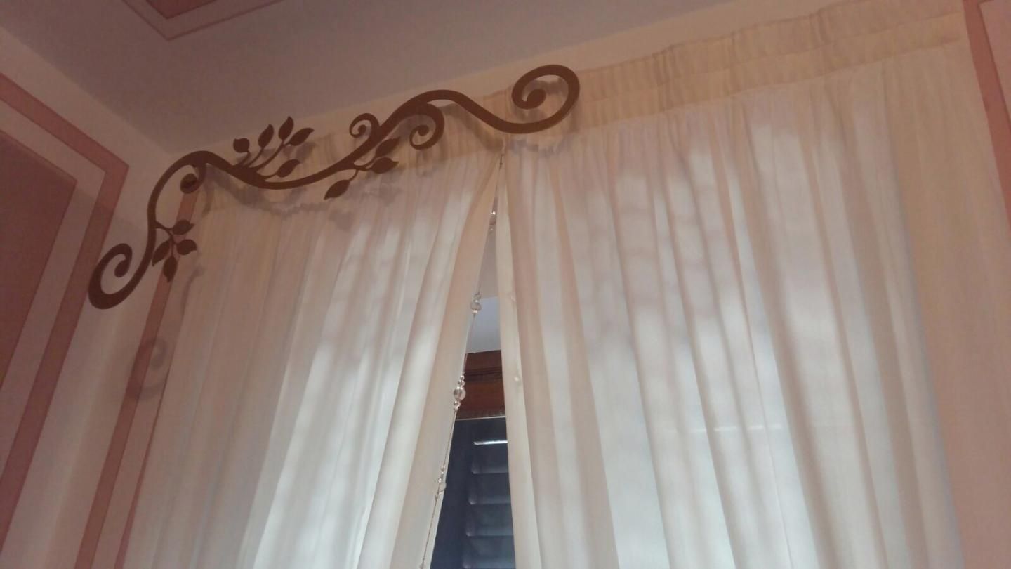 Un tralcio decorativo in metallo marrone scuro, con motivi a volute, è montato sopra tende bianche lunghe fino al pavimento.