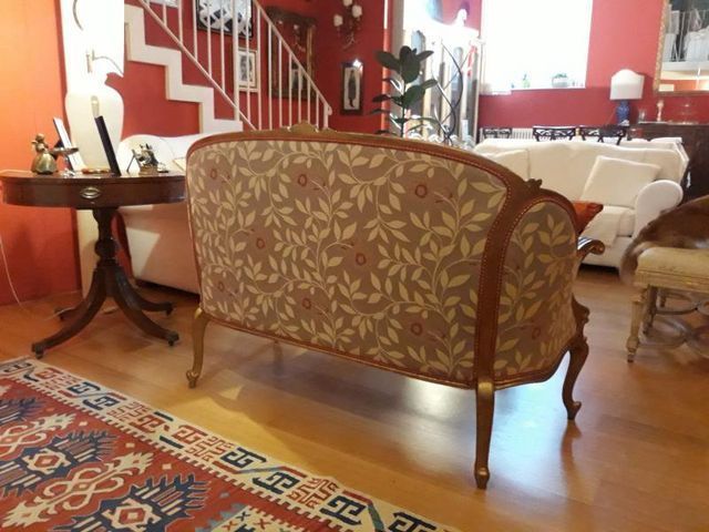 In una stanza con un tavolino rotondo, un tappeto e altri mobili, si trova un divanetto decorato con gambe in legno intagliato.