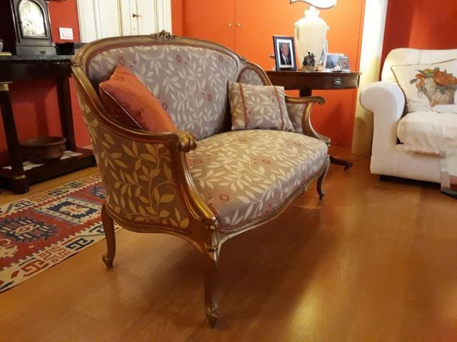 Un divanetto in stile vintage con tessuto a fantasia e legno intagliato e dipinto d'oro, collocato in una stanza con pareti arancioni e un tappeto.