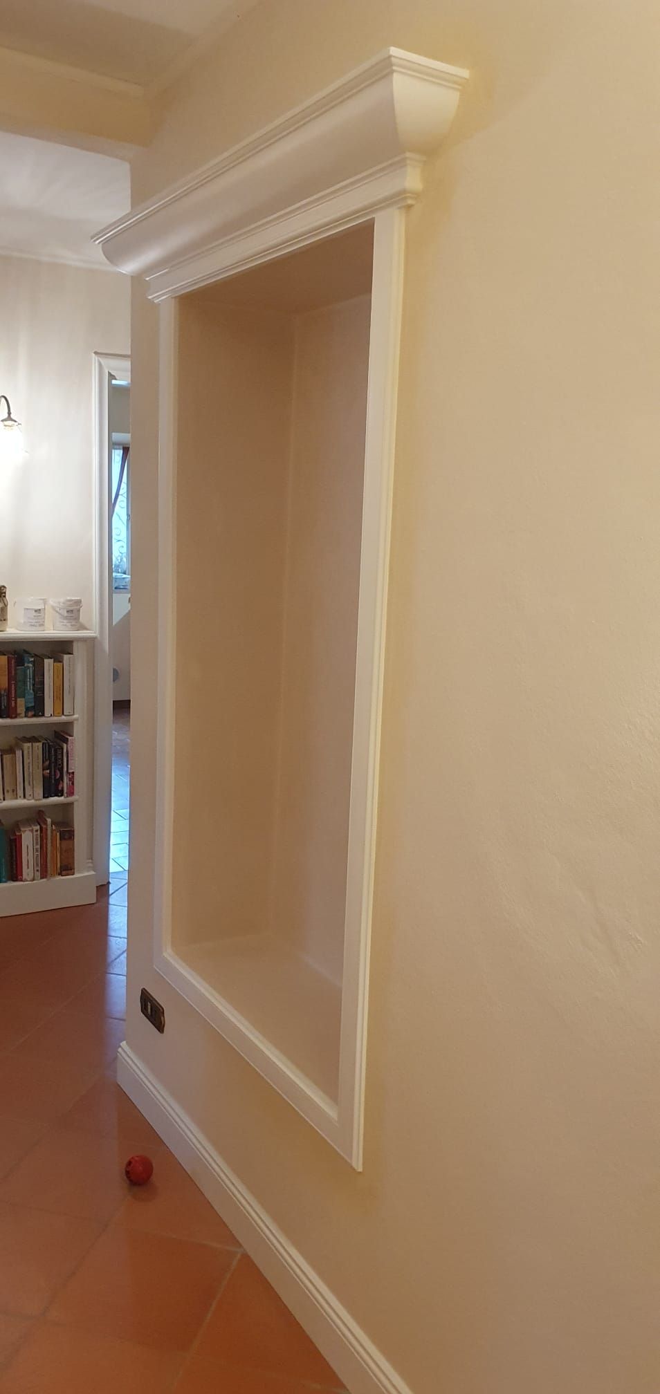 Una nicchia a muro incassata, rifinita con una modanatura decorativa bianca e cornici, su una parete di colore chiaro.