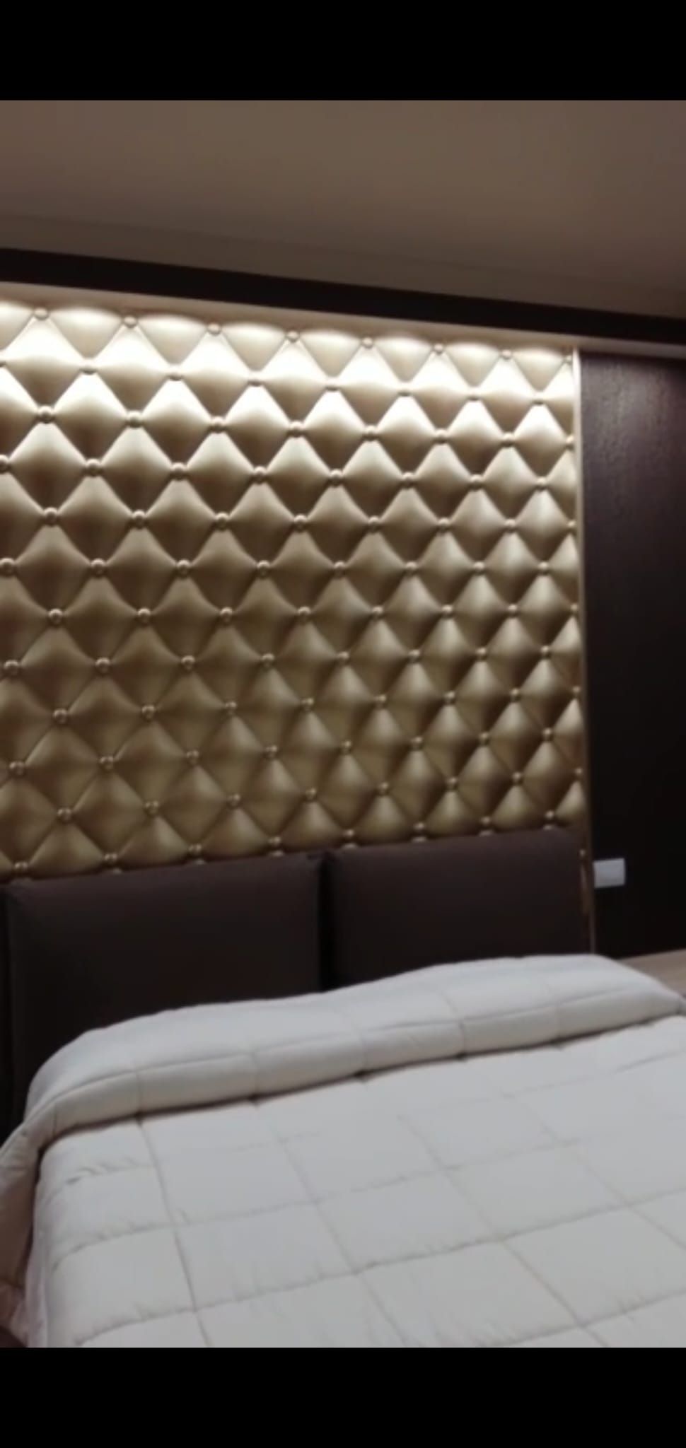 Una camera da letto moderna con una testiera imbottita color oro e trapuntata e un letto con lenzuola bianche.