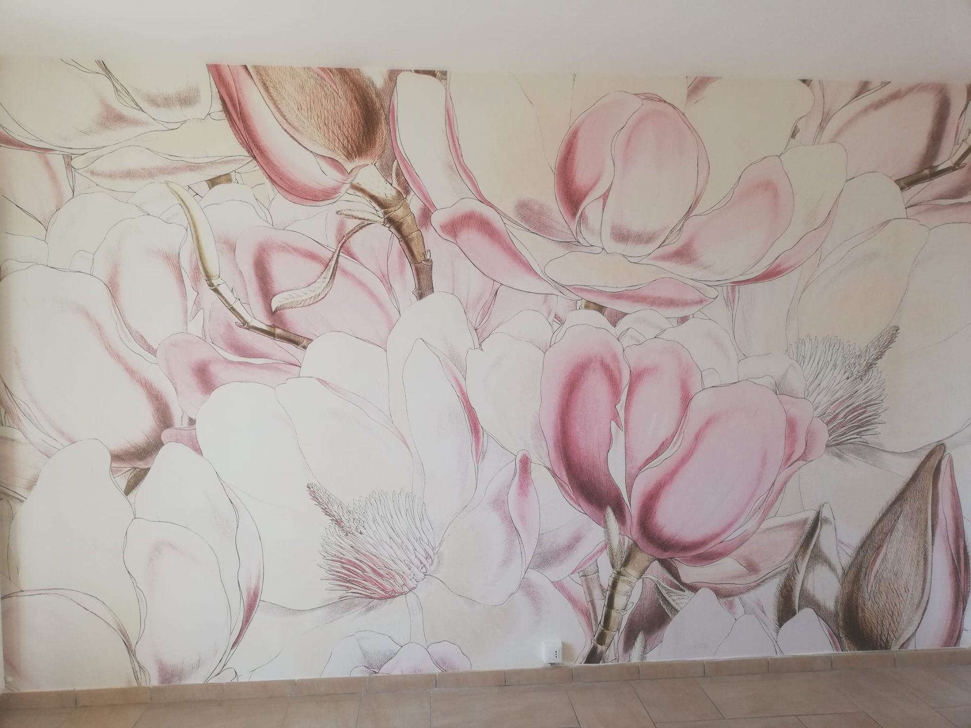 Un grande murale raffigurante delicati fiori di magnolia dipinti in tonalità di rosa cipria, bianco e marrone su una parete color crema.