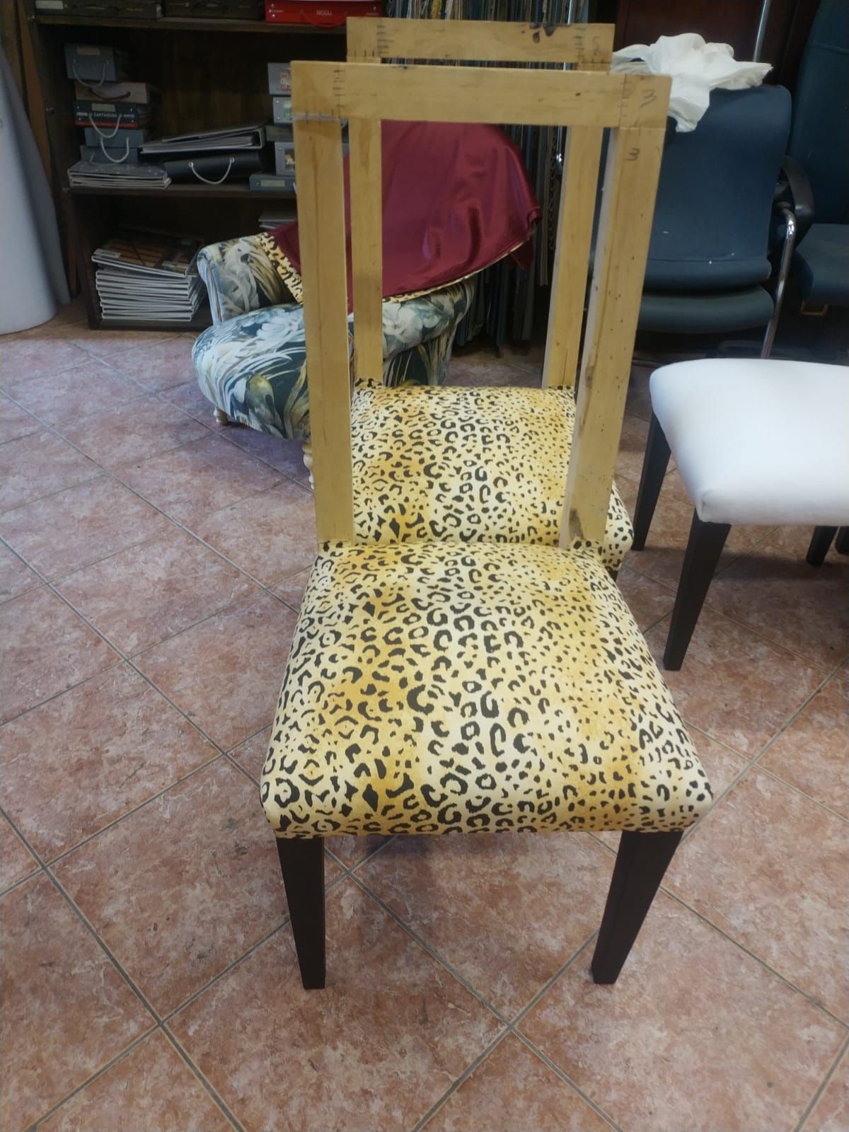 In un laboratorio, la struttura di una sedia con stampa leopardata è posizionata accanto ad altri mobili e campioni di tessuto su un pavimento piastrellato.