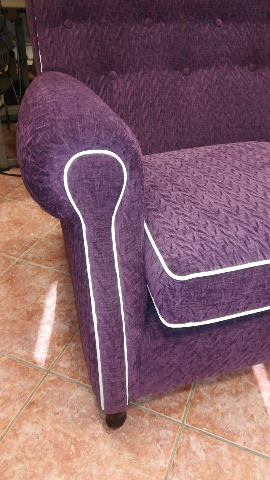 Una poltrona viola con rivestimento in tessuto testurizzato, caratterizzata da un'evidente bordatura bianca lungo i braccioli e il cuscino della seduta.