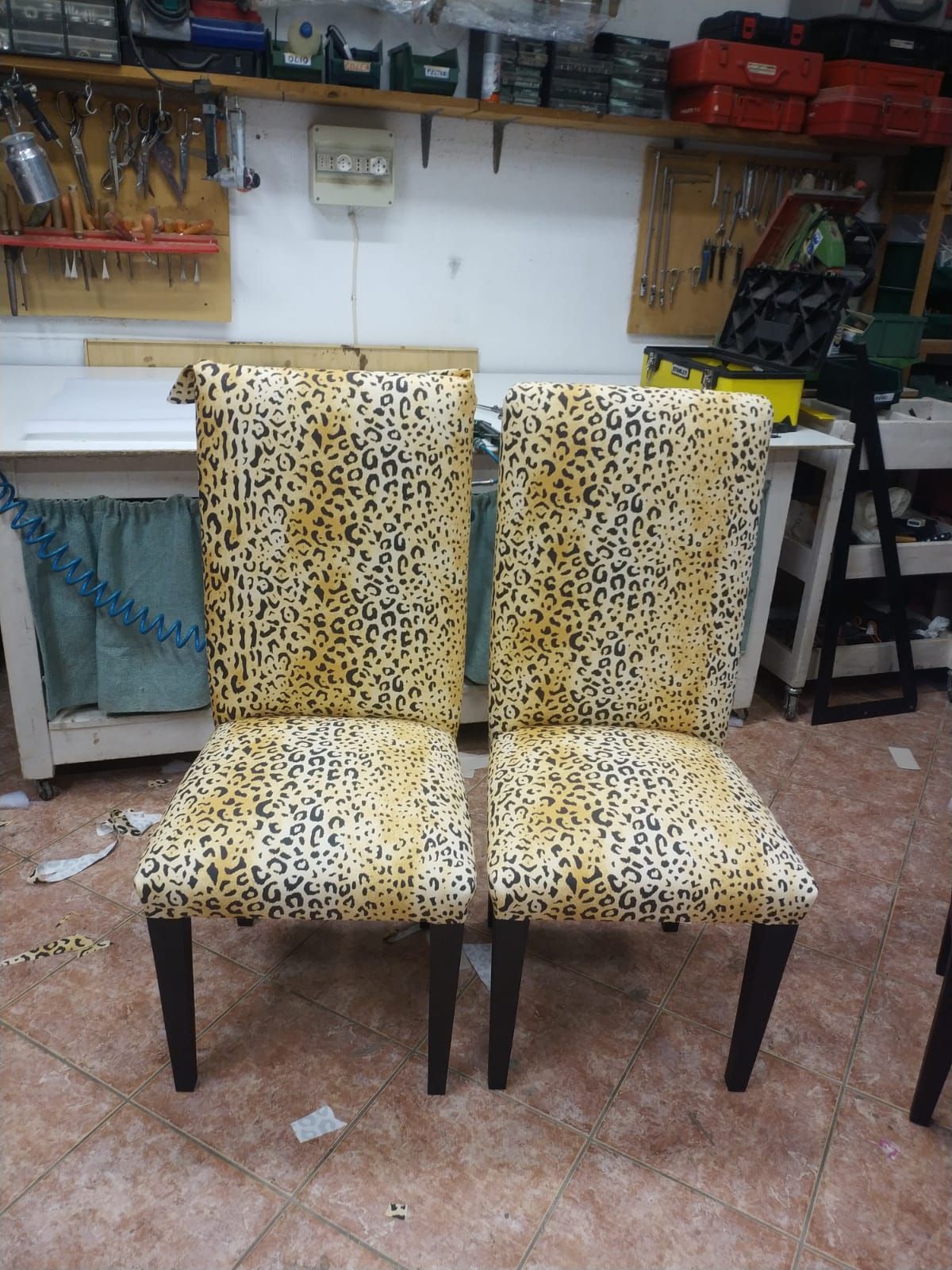 In un'officina, due sedie con rivestimento in tessuto leopardato e gambe in legno scuro sono posizionate una accanto all'altra.