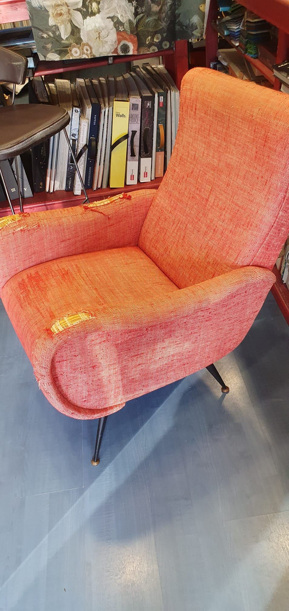 Una poltrona in stile moderno di metà secolo, di colore arancione con una texture particolare e gambe sottili in metallo, poggiata su un pavimento grigio.