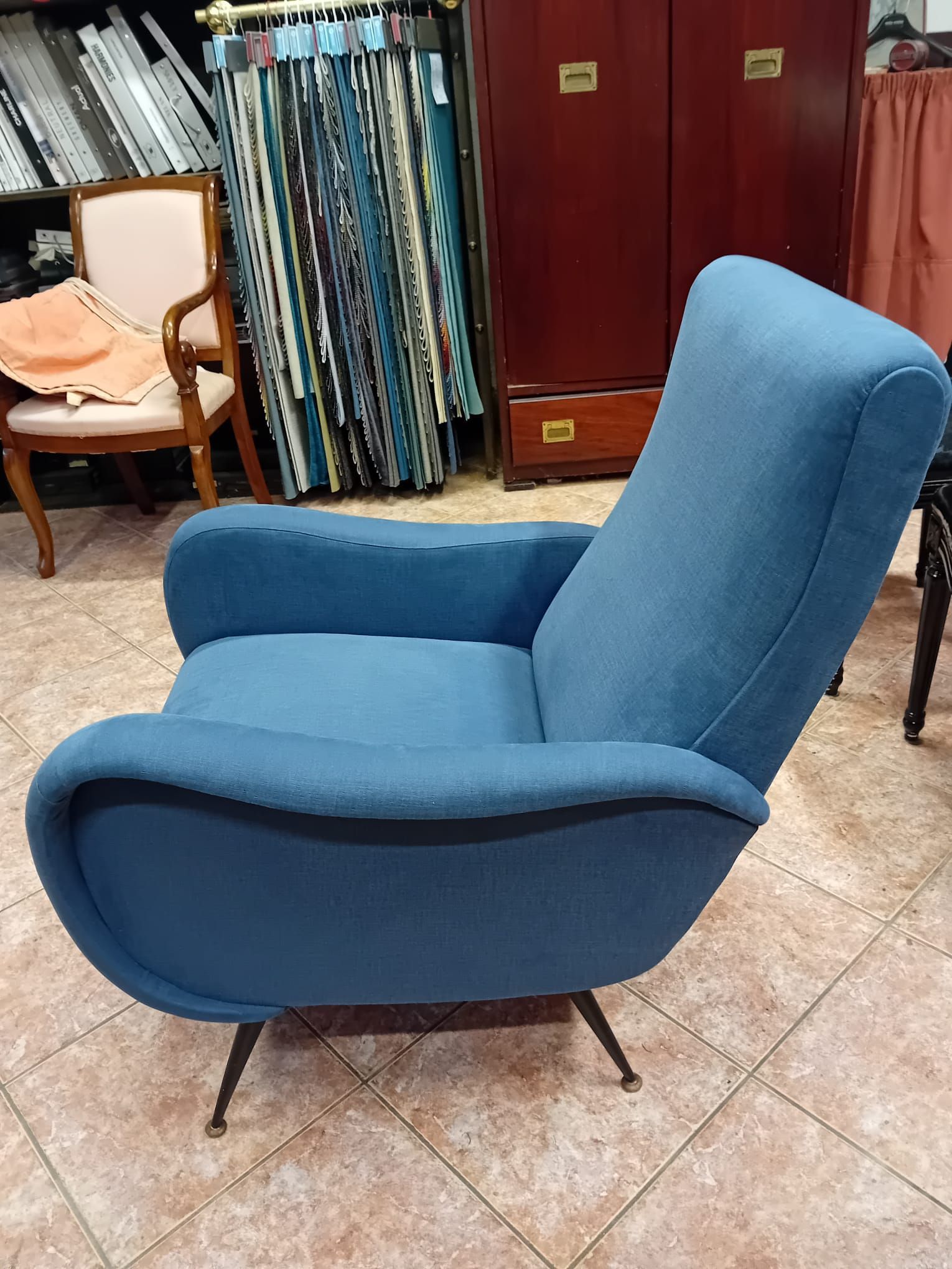 Una poltrona imbottita blu in stile moderno di metà secolo con gambe sottili e affusolate in metallo, esposta in uno showroom.