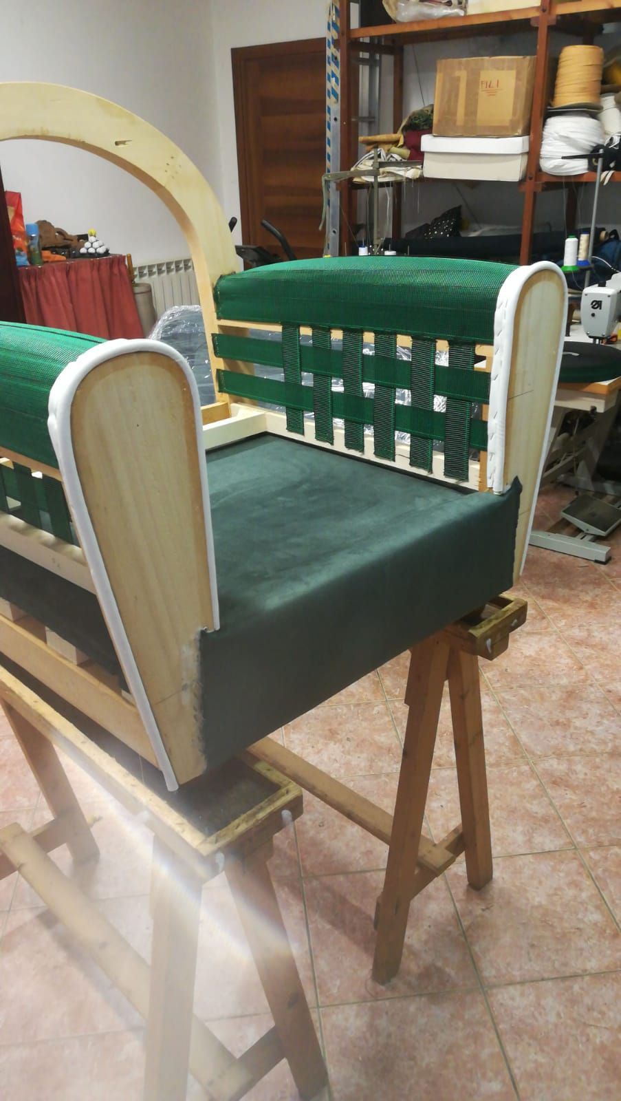 In un'officina, la struttura di una sedia imbottita con cinghie verdi è appoggiata su un banco da lavoro in legno.