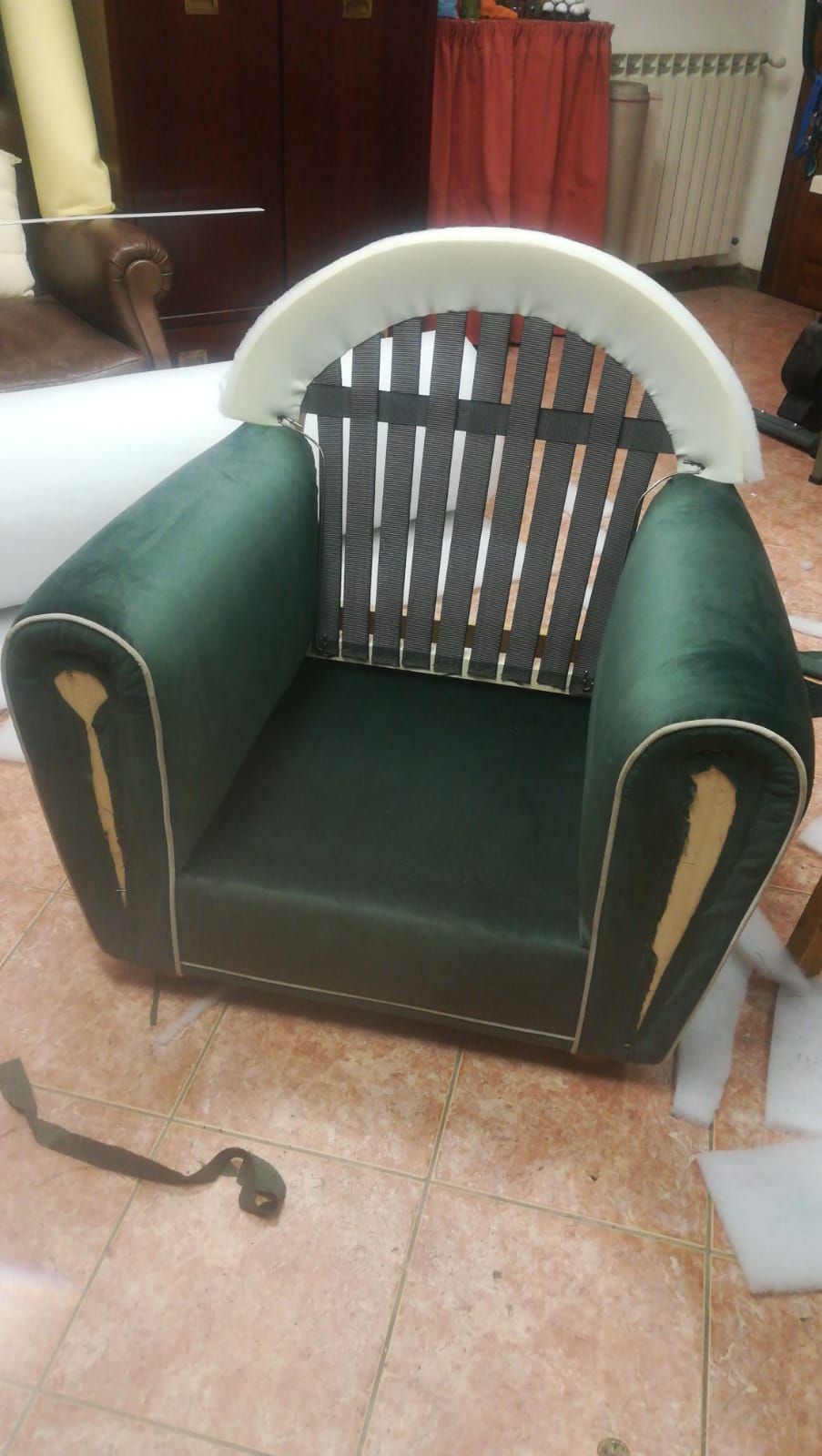 Una poltrona in velluto verde non rifinita con schienale a doghe di legno parzialmente a vista e profili color crema, collocata in una stanza.