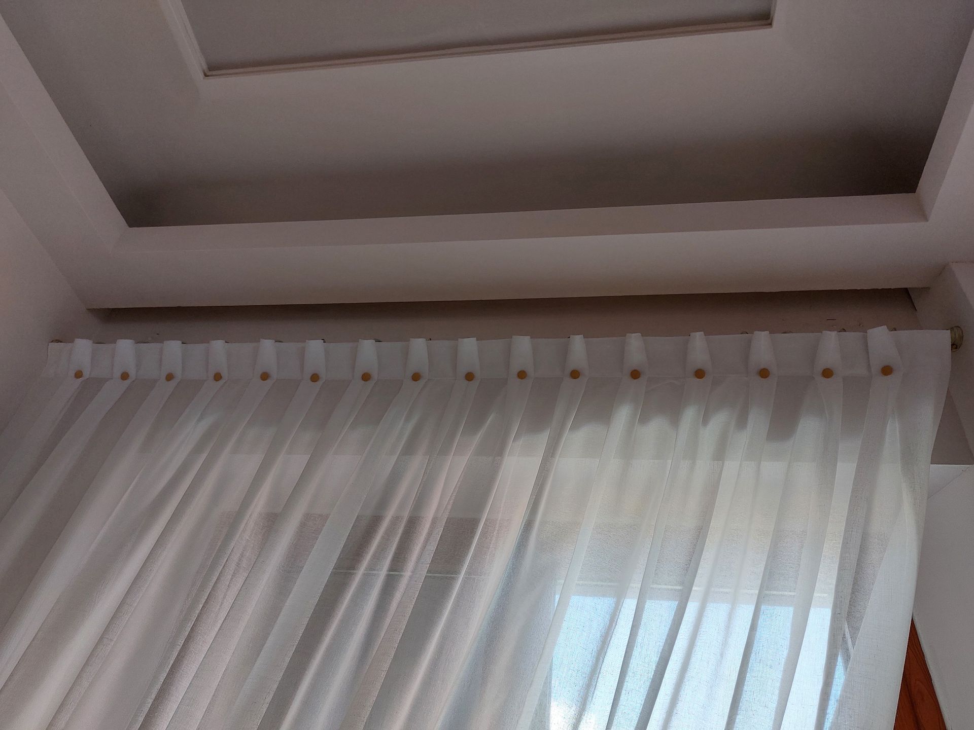 Tende bianche trasparenti, appese a un binario, incorniciavano un moderno soffitto a cassettoni.