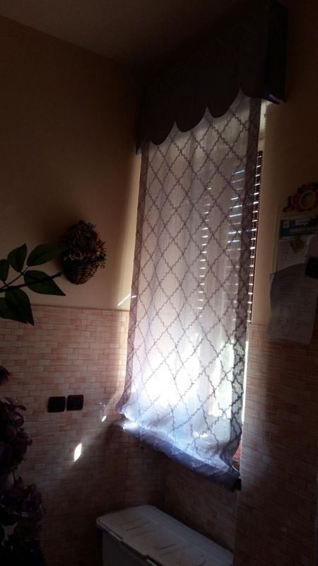 Una tenda filtrante con motivo a rombi è appesa a una finestra accanto a una parete piastrellata e a un ornamento decorativo.