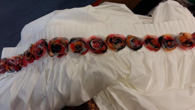 Una superficie di tessuto bianco plissettato decorata con una fila orizzontale di piccole rose decorative in tessuto multicolore.