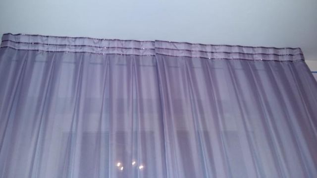 Delle tende trasparenti color lilla chiaro pendevano da un'asta per tende contro una semplice parete bianca.