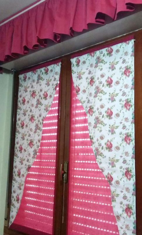 Una finestra con tende a stampa floreale, una mantovana rosa e persiane plissettate rosa che coprono parzialmente il vetro.