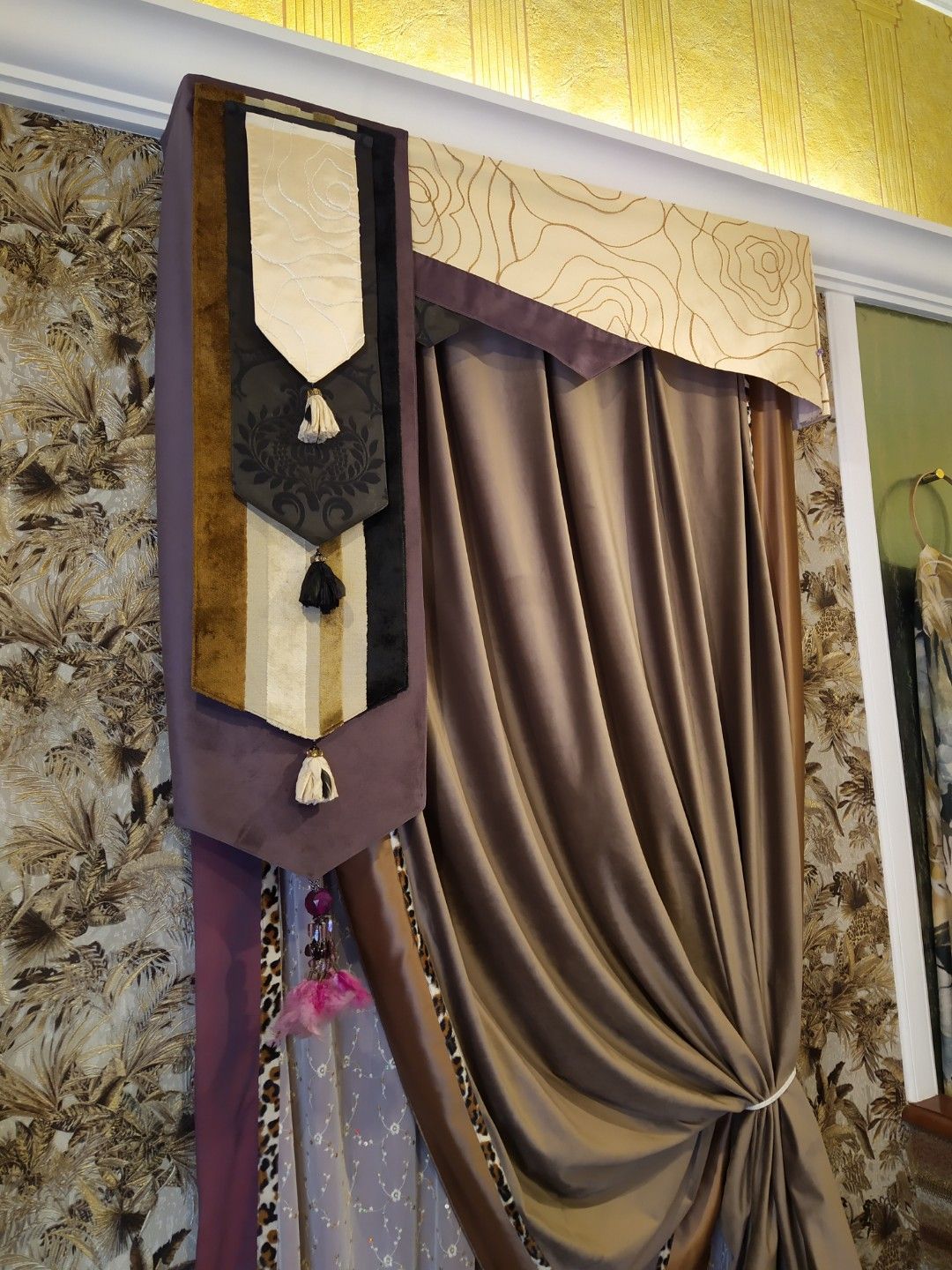 Eleganti tende per finestre con un pannello drappeggiato color tortora, una mantovana superiore a fantasia e un drappeggio laterale a più strati con nappe.