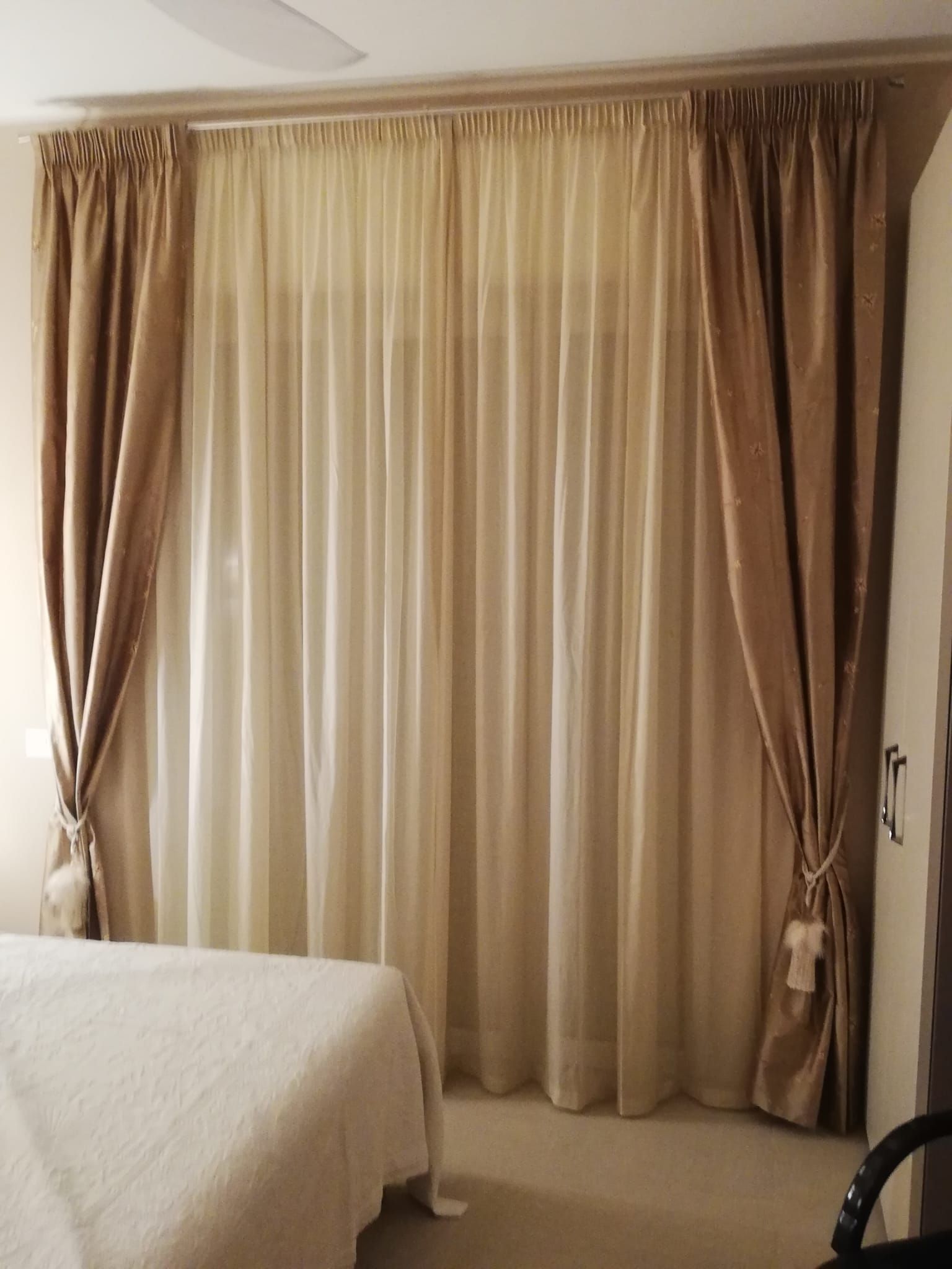 In una camera da letto, tende trasparenti beige che filtrano la luce, sovrapposte a tende color cuoio a tinta unita.