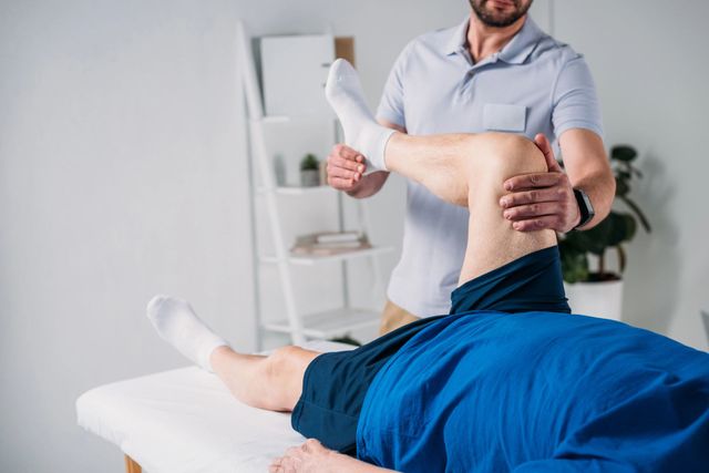 Un fisioterapista esegue esercizi di stretching sulla gamba di un paziente sdraiato su un lettino da trattamento in una luminosa stanza della clinica.