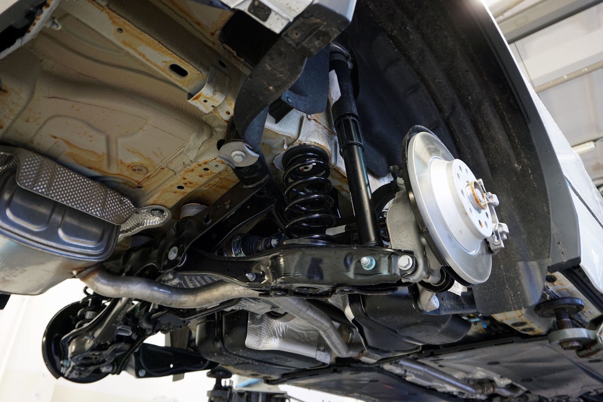 Undercarriage of a vehicle, showing suspension, brakes, and exhaust system. Black, gray, and silver components.