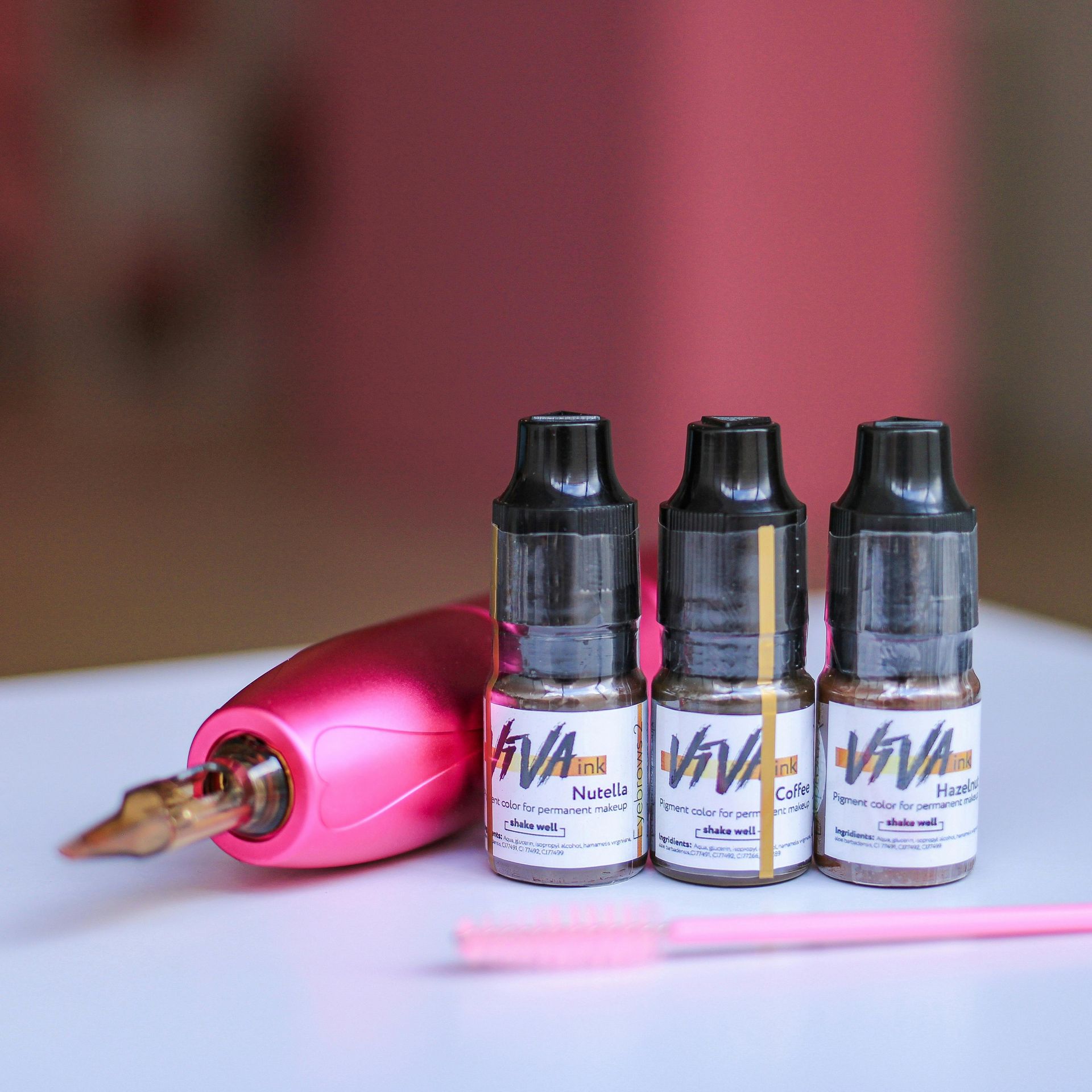 Three Viva ink bottles and a pink tattoo pen with a mascara wand on a white surface.