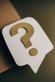 A gold question mark sits on a white, speech bubble-shaped cutout against a dark, textured background.