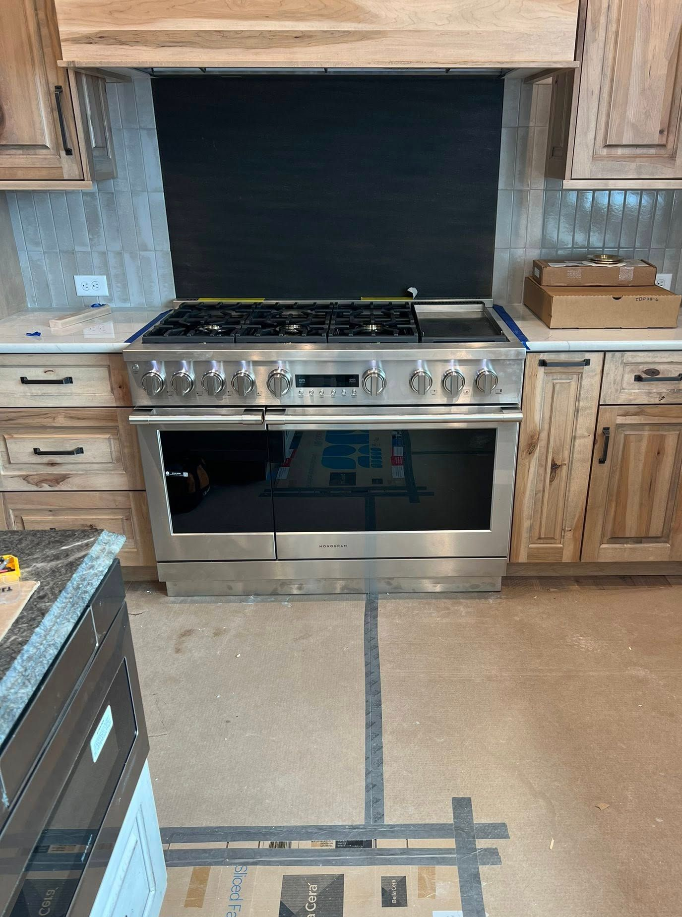 Stainless steel range in a kitchen, with wooden cabinets, black backsplash, and light-colored floor.