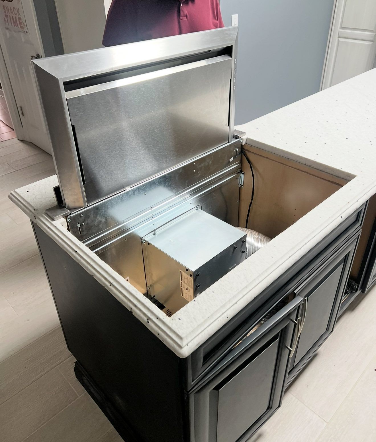 Kitchen island with pop-up range hood open, revealing the internal workings. Stainless steel and dark cabinets.