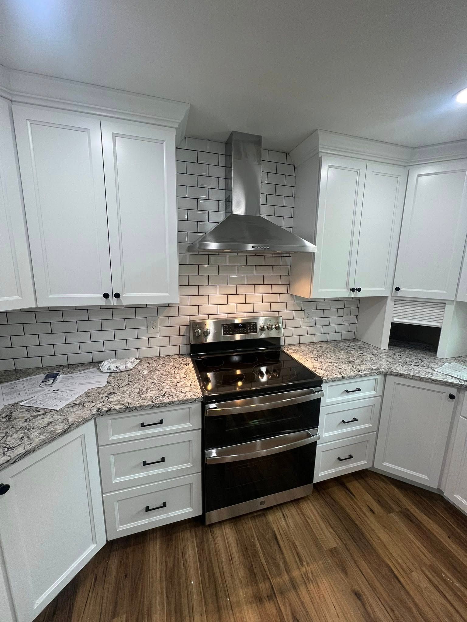 White kitchen with stainless steel appliances, granite countertops, and wood floors.