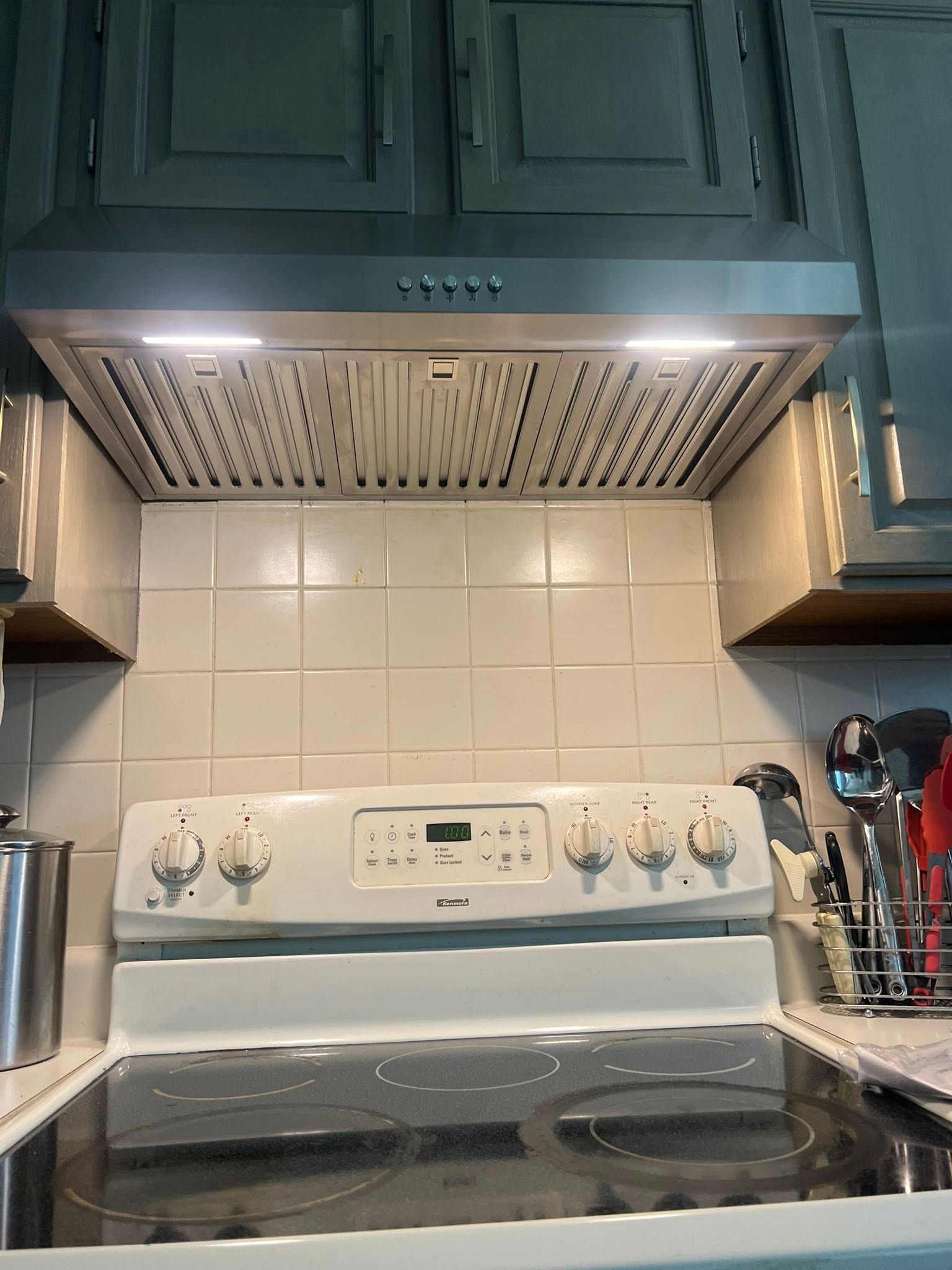 Kitchen with stove, vent hood, white tile backsplash, and cabinets.