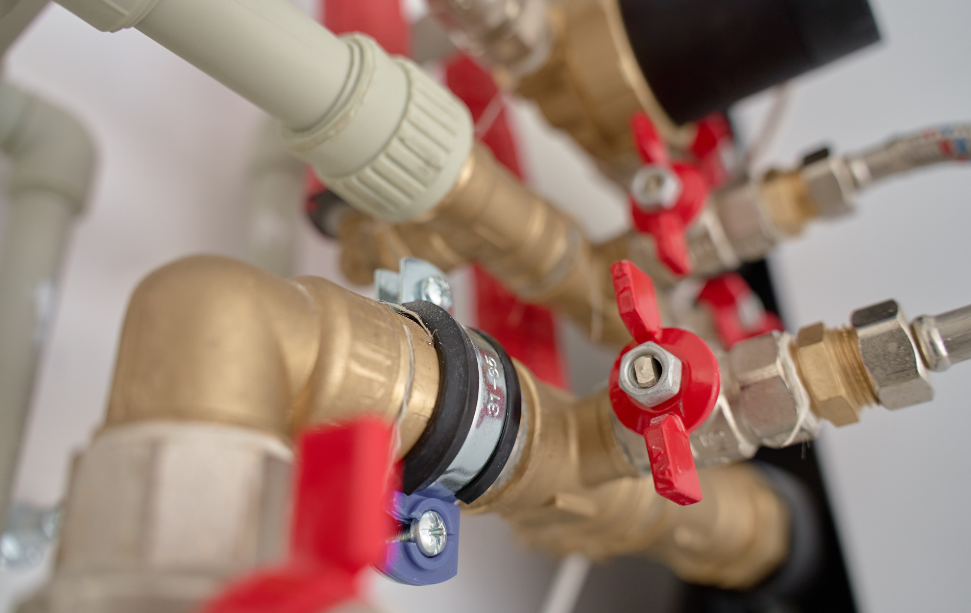 Close-up of plumbing pipes and valves, with red handles, against a white wall.