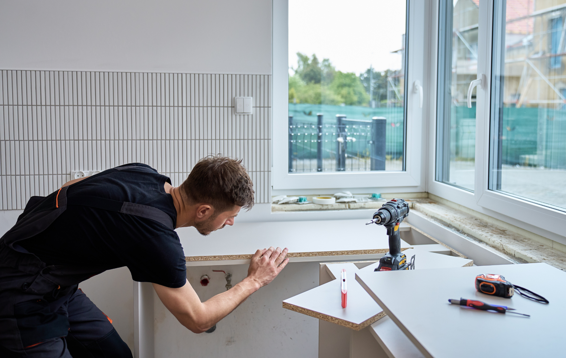 Man installing a countertop in a kitchen, using a drill and measuring tape.
