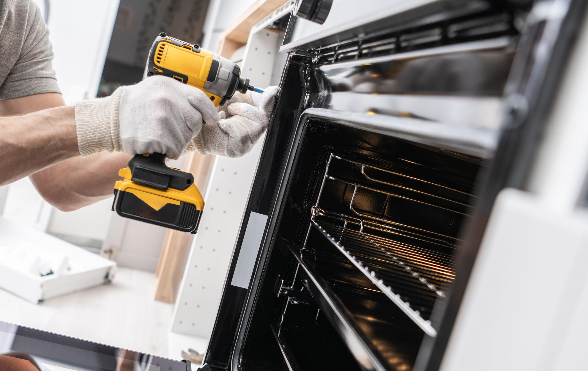 Person in gloves using a yellow drill to repair an oven.