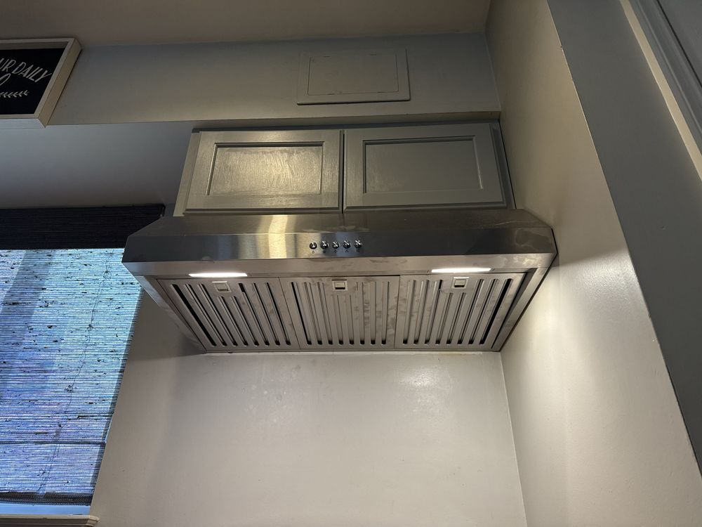 Stainless steel kitchen range hood with cabinets above, mounted on a white wall.