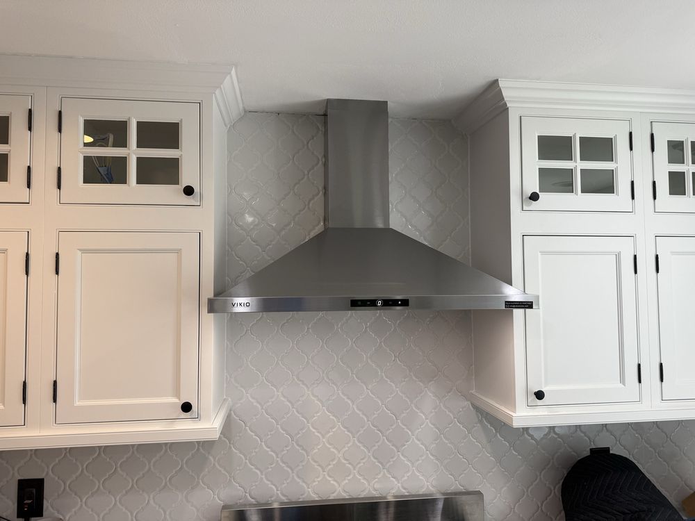 Stainless steel range hood centered between white kitchen cabinets. White tile backsplash.
