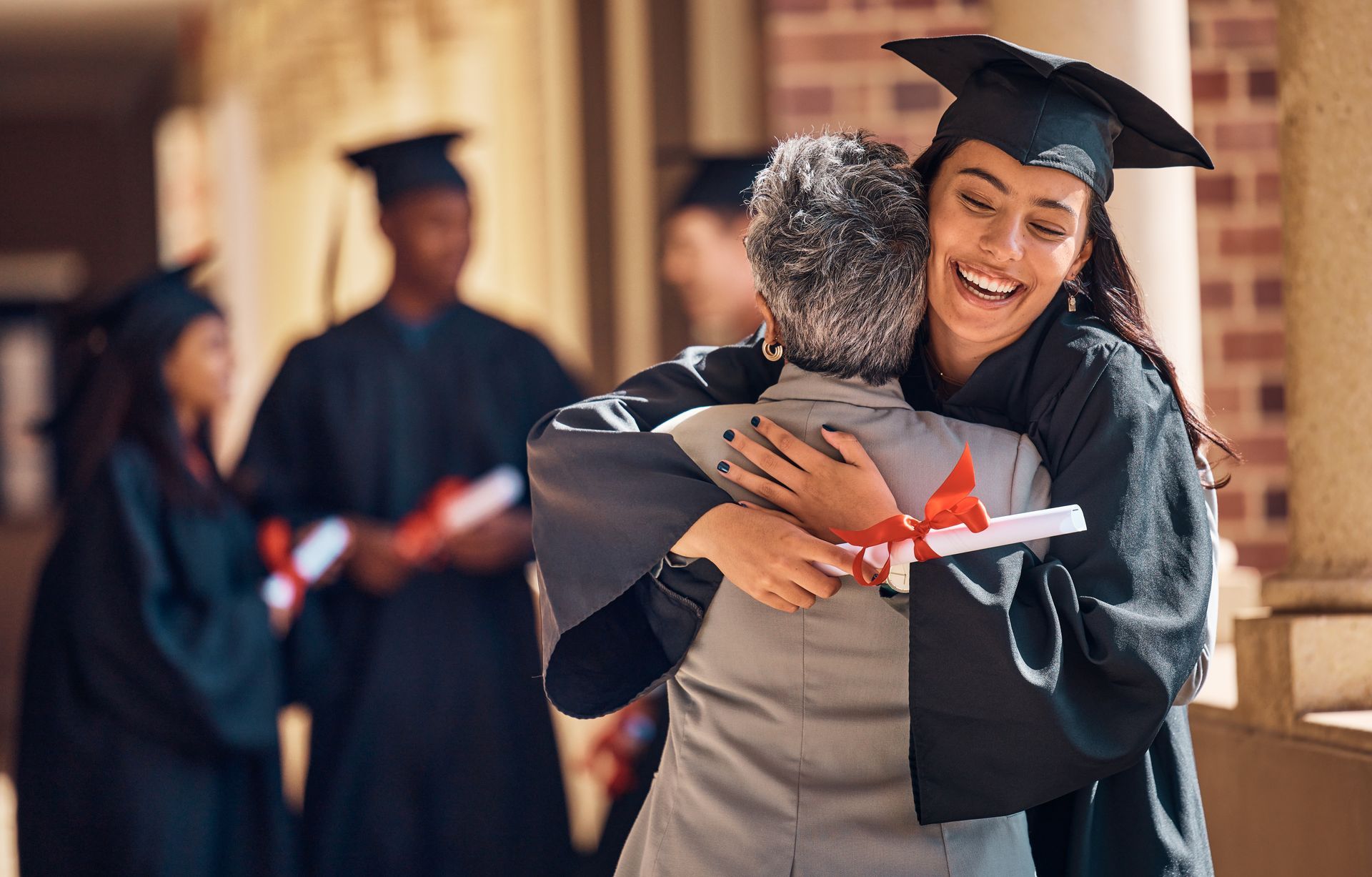Stock photo of a graduate hugging a relative and holding a diploma