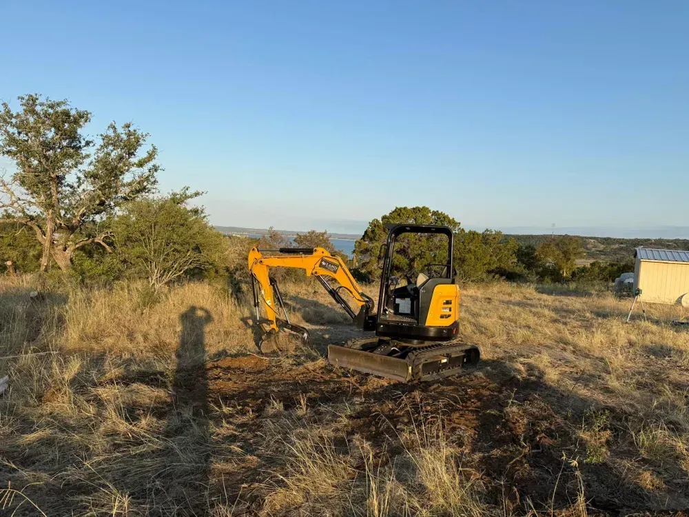 A small yellow excavator is sitting in the middle of a field.