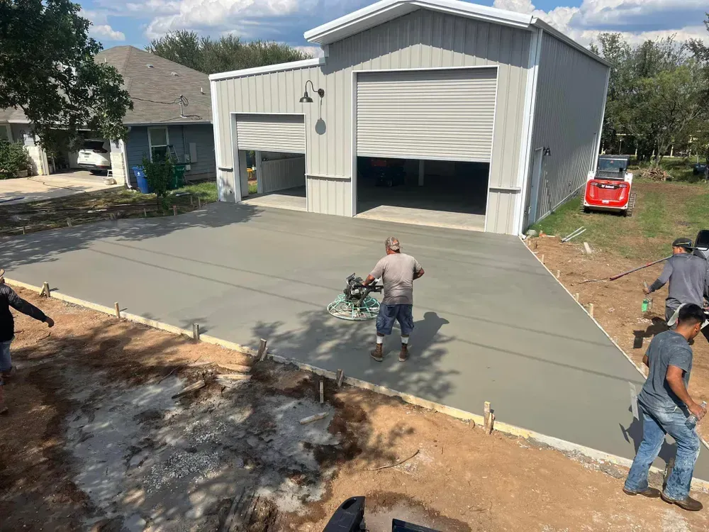 A group of men are working on a concrete driveway in front of a garage.