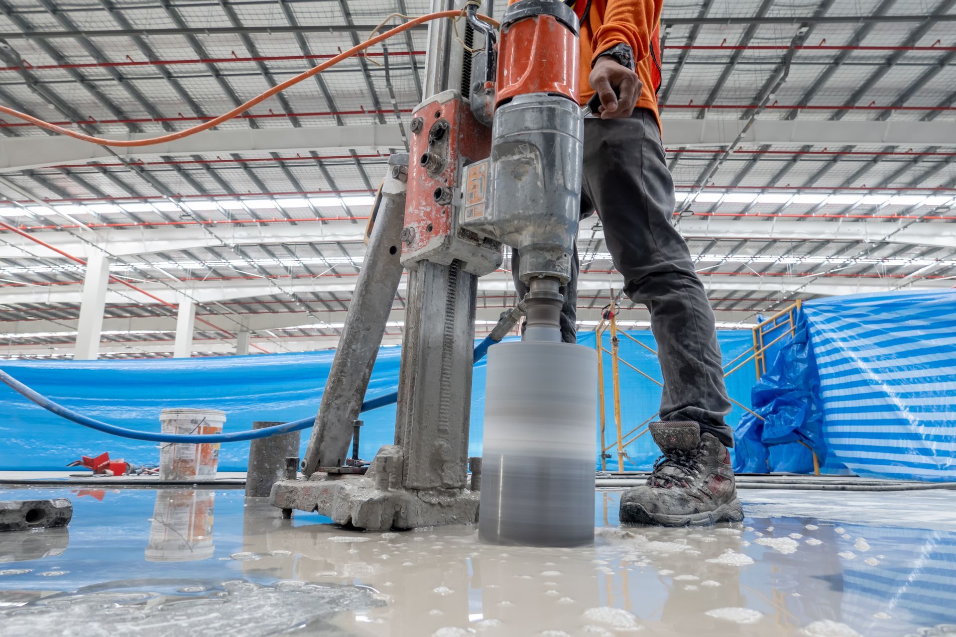 A construction worker is drilling holes in the floor of a building.