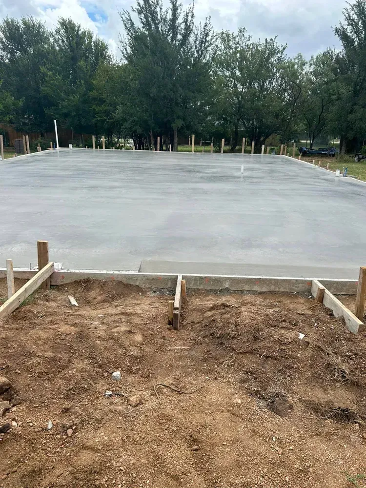 A concrete foundation is being built in a yard with trees in the background.