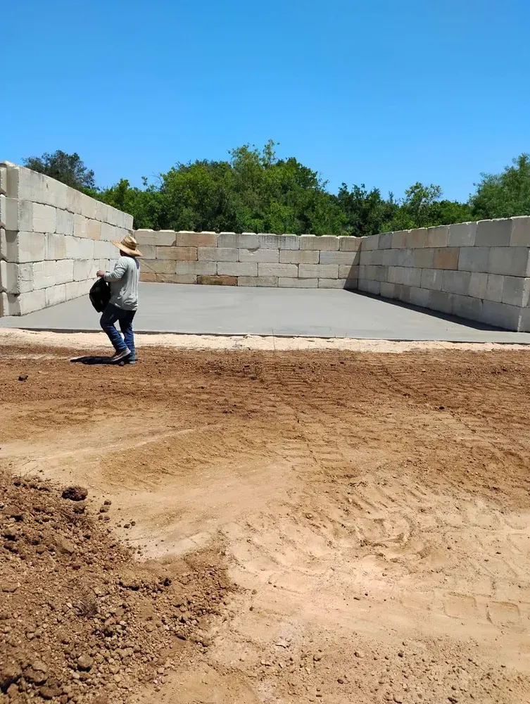 A man is standing in a dirt field in front of a concrete wall.