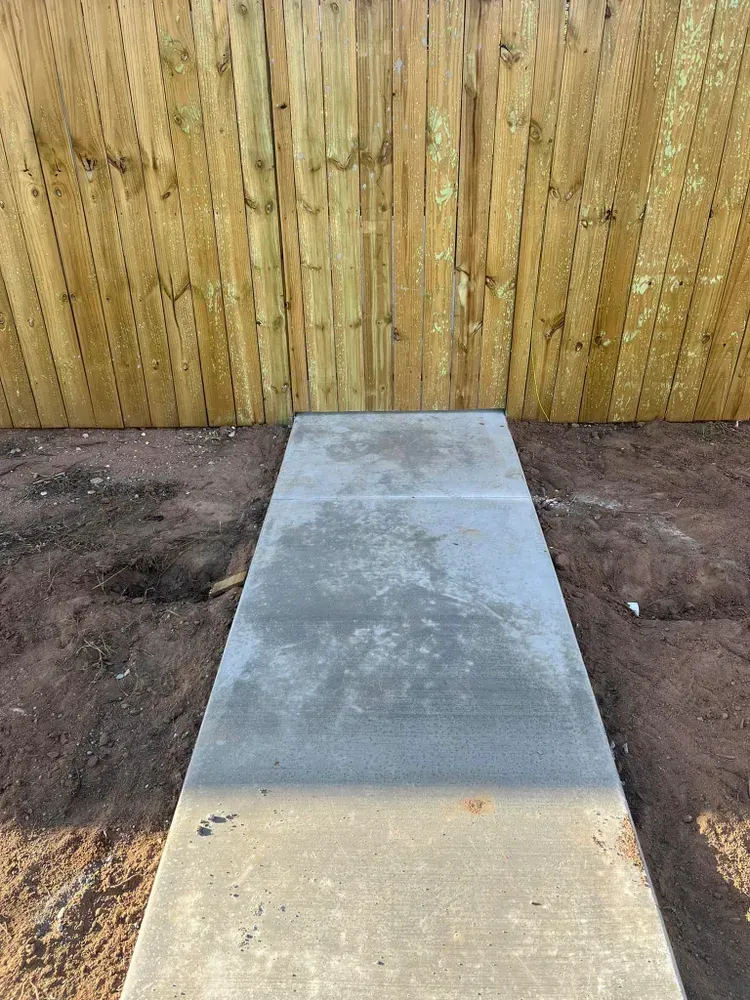 A concrete walkway leading to a wooden fence in a backyard.