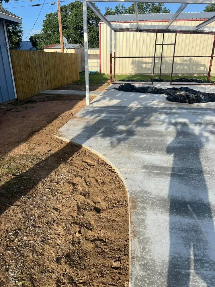 A shadow of a person is cast on a concrete surface in a backyard.